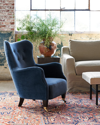 Tufted chair in front on a side table with a pot with plants behind it. Photographed in Lucas Shadow.