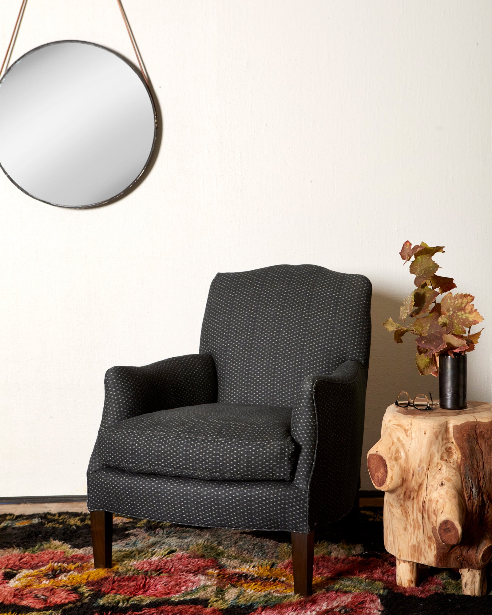  Navy blue dotted armchair in a room with a round mirror and a wooden side table with decorative elements. Photographed in Tori Indigo. 