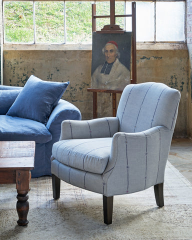 Striped blue chair in front of a painting and next to a blue sofa. Photographed in Fatima Mist.