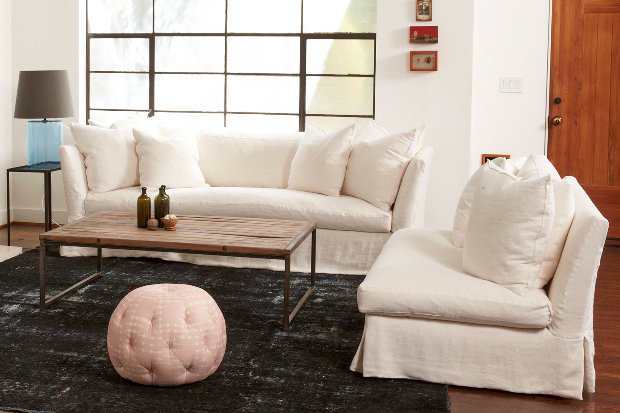  White sofa and loveseat in a living room with a wood coffee table and pink pouf. Photographed in Brevard Ivory. 