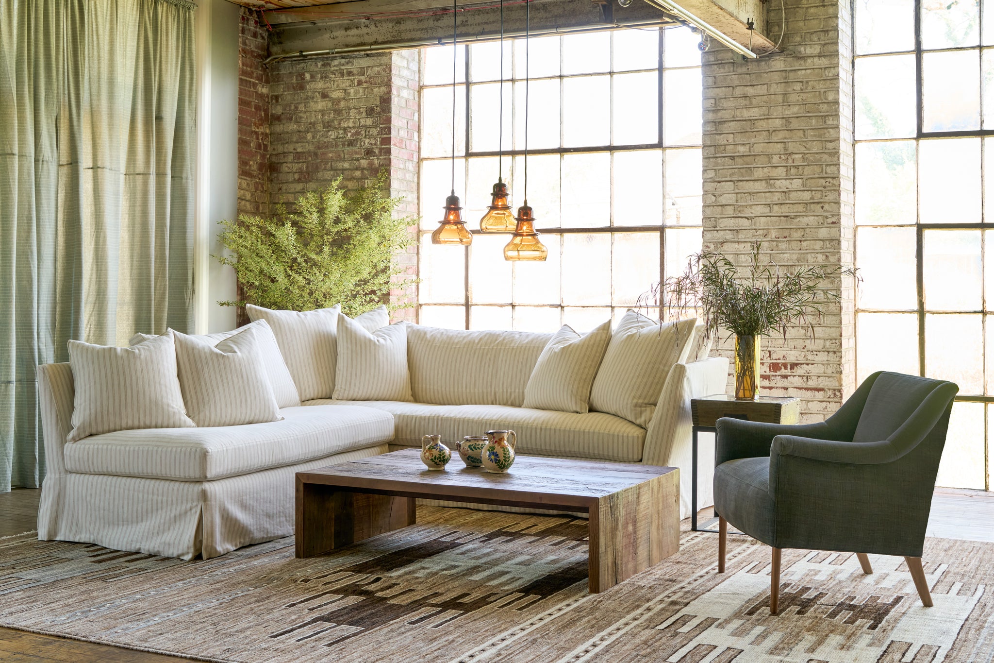  Striped sectional with a wood coffee table on a brown rug. 3 brown glass pendants and a black chair on the right. Photographed in Rye Black. 