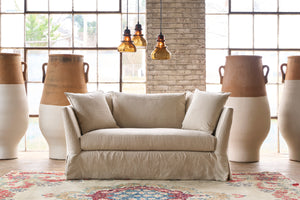  Loveseat in front of a wall and windows with large painted pots. 3 brown glass pendants are hanging. Photographed in Noah Bone. 