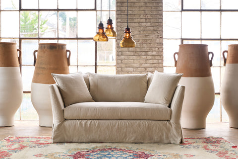 Loveseat in front of a wall and windows with large painted pots. 3 brown glass pendants are hanging. Photographed in Noah Bone.