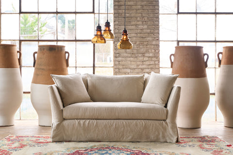 Loveseat in front of a wall and windows with large painted pots. 3 brown glass pendants are hanging. Photographed in Noah Bone.