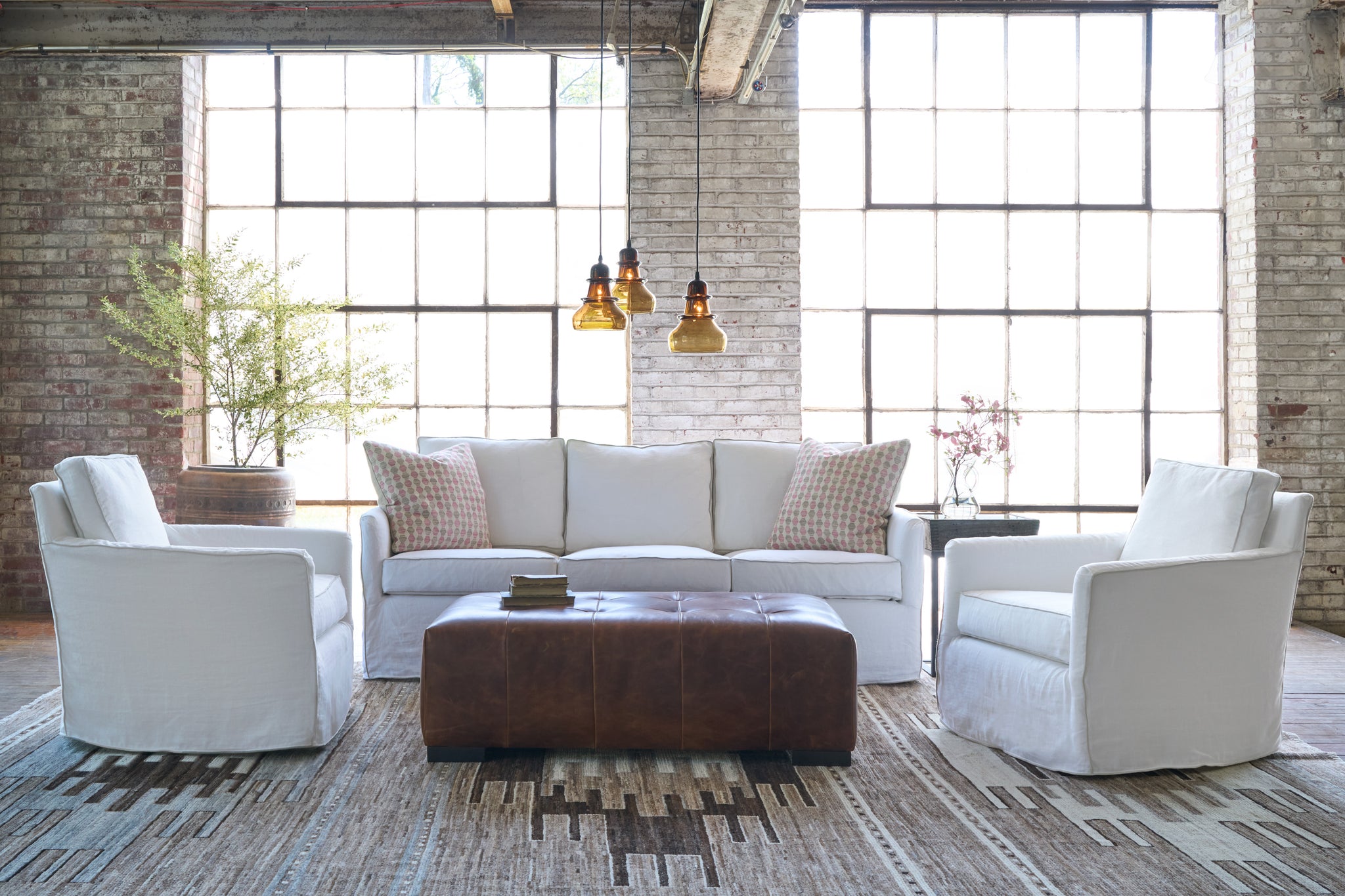  White sofa in a showroom with 2 white chairs. Brown leather ottoman on a brown and beige carpet. 3 brown glass pendants. Photographed in Ashville. 