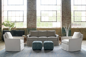  Grey sofa in a showroom with 2 white chairs and 2 square ottomans with floral fabric. Photographed in Anemone Marine Blue. 