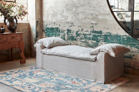 Daybed with a blue rug next to a wood credenza with a pot with branches. Photographed in Brevard Mist.
