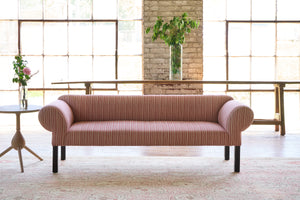  Striped sofa in front of large windows with a side table with flowers on top. Photographed in Hickory Persimmon. 