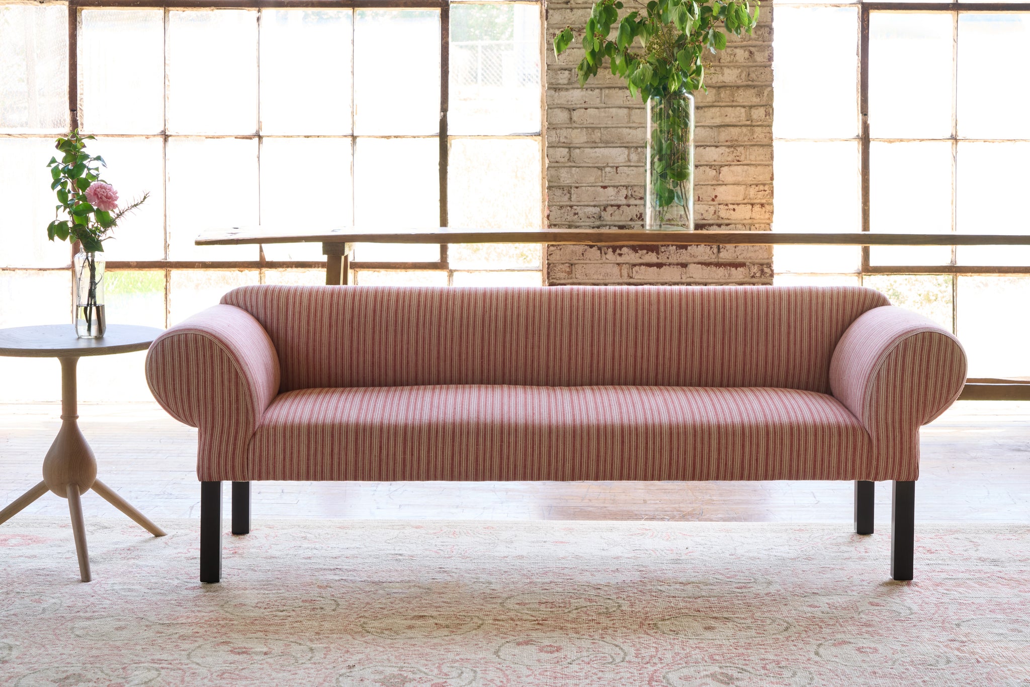  Striped sofa in front of large windows with a side table with flowers on top. Photographed in Hickory Persimmon. 