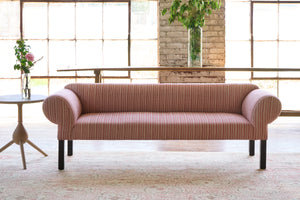  Striped sofa in front of large windows with a side table with flowers on top. Photographed in Hickory Persimmon. 