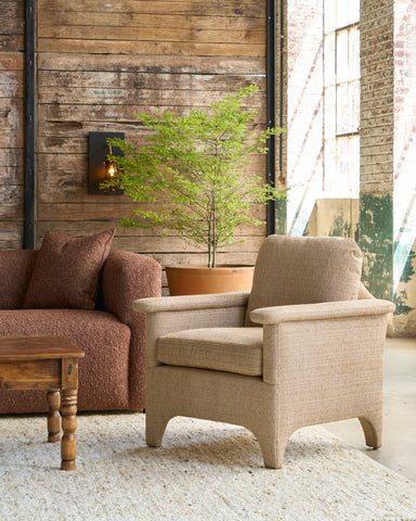 Beige armchair in a room with wooden walls and a large window. Photographed in Reed Gold.