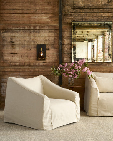 Slipcovered chair in front of a wood wall. Photographed in Brevard Birch.