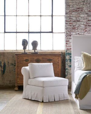  White chair with box pleat by a bed. Photographed in Luna White. 