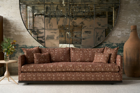 Brown patterned sofa in a room with a large round mirror and decorative vase. Photographed in Foret Rust.