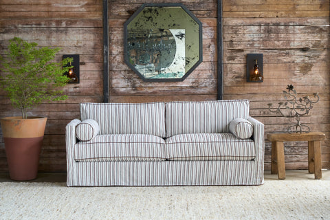 Striped sofa in front of a wood wall with a mirror and a planter on the left. Photographed in Bridget Chestnut.