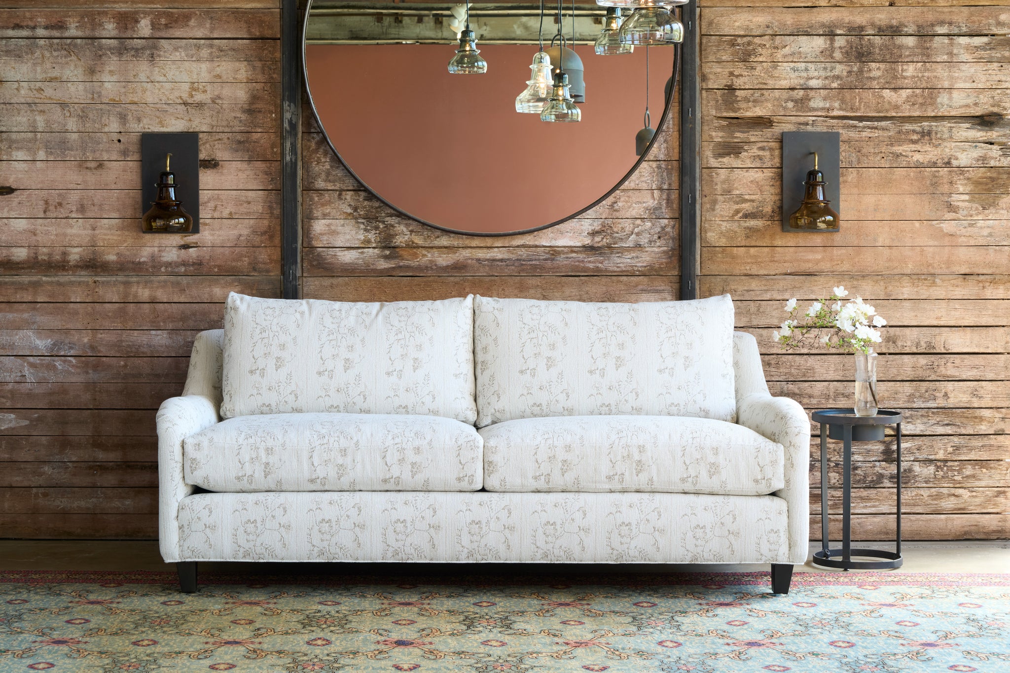  White sofa in front of a wood wall with a round mirror on the wall. Photographed in Foret Ivory. 