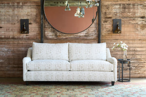  White sofa in front of a wood wall with a round mirror on the wall. Photographed in Foret Ivory. 
