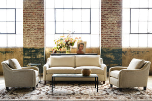  Sofa in a cream color linen in front of windows with a chair on each side and a mirrored coffee table in the middle. Photographed in Bellamy Oatmeal. 