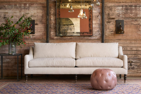 Beige sofa in a room with wooden walls, a patterned rug, and decorative elements. Photographed in Sadie Flax.