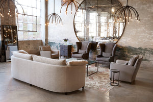  The Havana sofa is upholstered in Bellamy Oatmeal, in a large showroom setting with lots of natural daylight. There are Blossom chandeliers, 2 brown wing chairs against a wall with a very large Geller mirror. Two Stanford chairs are on the side of the sofa. You can see the back of the Havana sofa, showing its curved back. Photographed in Bellamy Oatmeal. 
