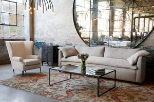  The Havana sofa is shown in Bellamy Oatmeal with a Melrose wing chair on the left in a cream colored linen. There is plenty of daylight, a metal and mirror coffee table and a very large round mirror on the back wall. The rug is green and read on a beige background. Photographed in Bellamy Oatmeal. 