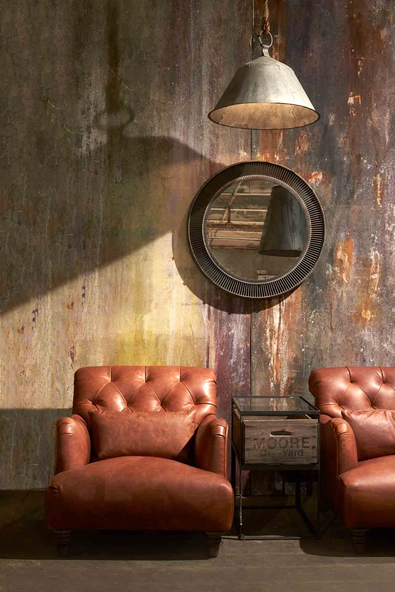  Leather chairs in Spur Terracotta next to a side table. Sitting in front of a colorful wall with a lamp and mirror hanging. Photographed in Spur Terracotta. 