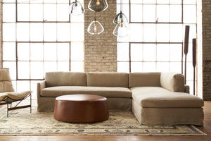  Allister Sectional in Brevard Burlap next to a leather ottoman. Photographed in Brevard Burlap. 