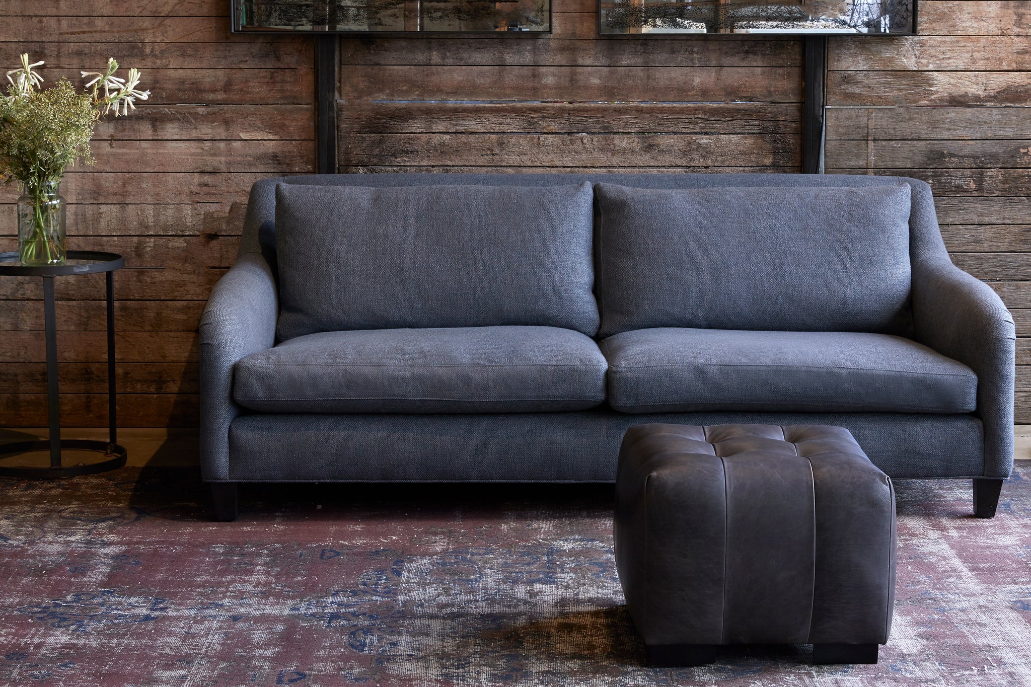  Arden Ottoman in Indiana Charcoal next to a blue sofa. Photographed in Indiana Charcoal. 