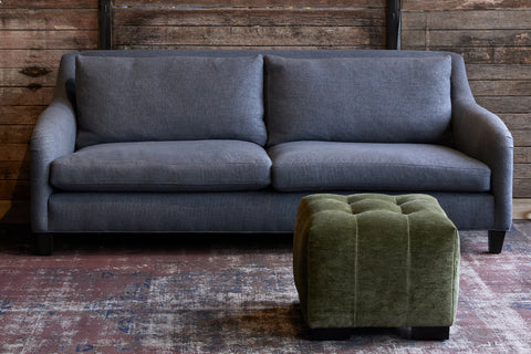 Arden Ottoman in Velluto Olive next to a blue sofa. Photographed in Velluto Olive.