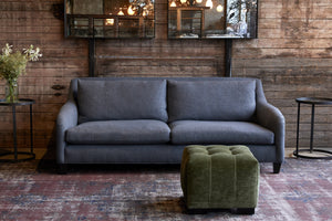  Arden Ottoman in Velluto Olive next to a blue sofa. Photographed in Velluto Olive. 