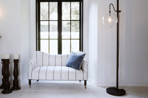  Small loveseat placed in front of large window in a white room with metal floor lamp. 
