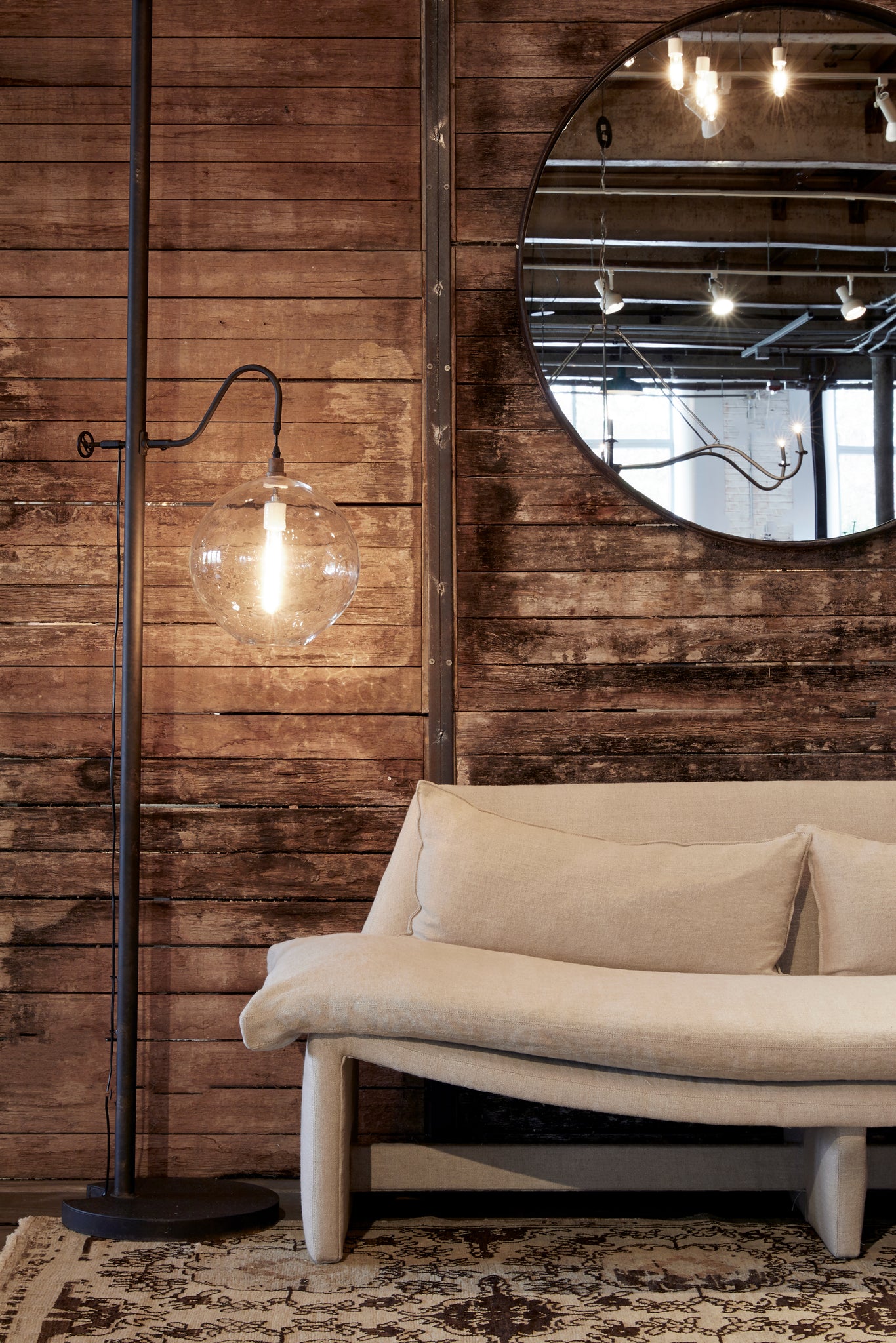  Metal floor lamp with clear circular pendant next to a sofa with neutral fabric sitting in front of a wood wall. 