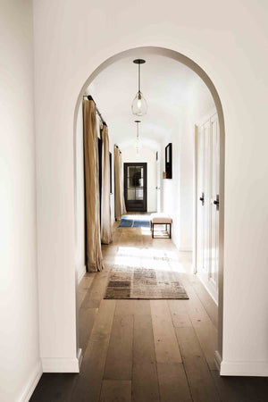  Hallway shot. Round archways, wood floors, neutral colored rug and curtains with clear oval pendants hanging from ceiling.  