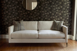  Light colored sofa with pillows in front of a dark wall and mirror. Front view. Photographed in Lucerne Vanilla. 
