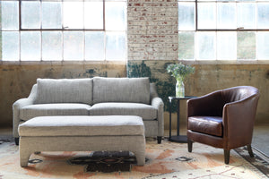  Grey sofa and bench in a showroom with a leather chair on the right. Photographed in Spur Chocolate. 