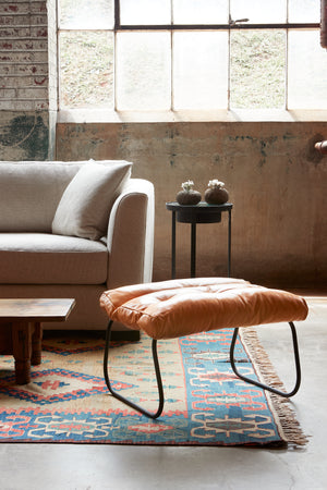  Brando Ottoman in Olivo Cashew next to a light sofa. Photographed in Olivo Cashew. 