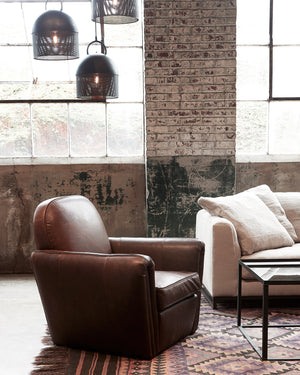  Dark colored chair next to a light sofa. In the background is a brick wall with two large glass windows. Photographed in Spur Chocolate. 