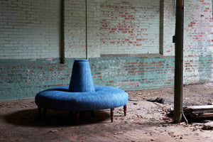  The Coin sofa is in a blue fabric with a pattern and is in a dark room with brick walls. 