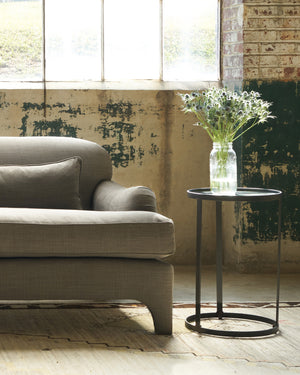  Side table on the right of a grey sofa. Flowers on top. 