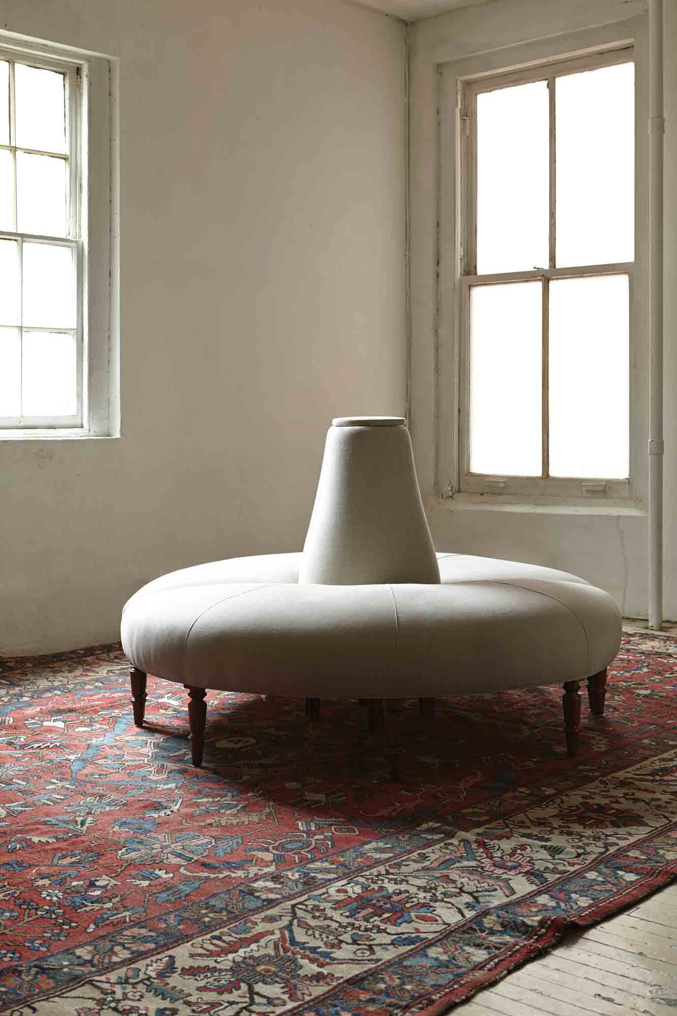  Round light colored sofa in a room with daylight coming through 2 windows, on a red rug with patterns. Photographed in Vintage Flax. 