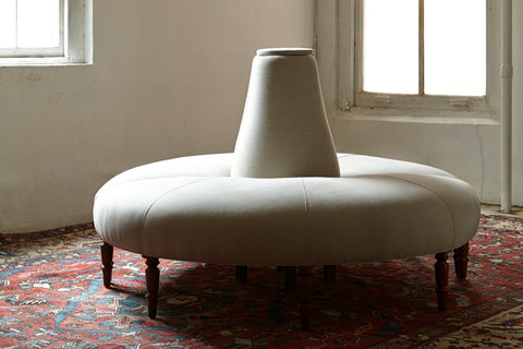 Round light colored sofa in a room with daylight on a red rug with patterns. Photographed in Vintage Flax.