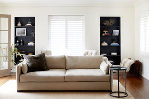  Daylight in a white living room with 2 black bookcases on the back wall. The sofa is in a natural color fabric with a round side table to the right. Photographed in Brevard Burlap 