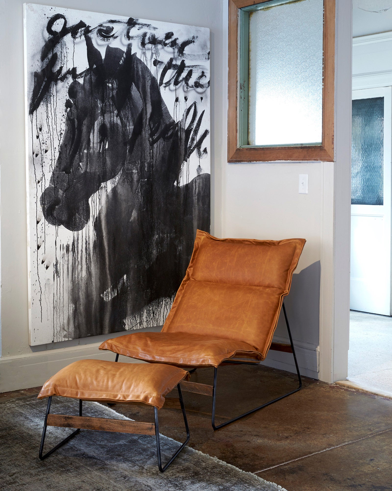  Chair in Olivo Cashew with matching ottoman. In the background is a light room with a dark horse painting and a window hanging. Photographed in Olivo Cashew. 