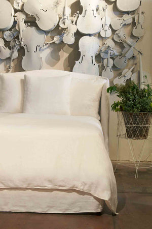  Emma bed in Otis White next to flower pot. In the background is a wall full white violins. Photographed in Otis White. 