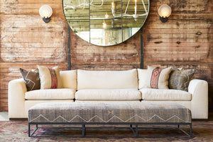  Lorenzo 3 piece Sofa in front of a wood wall with 2 white Emma Sconces. Large brown kilim bench in front. There are 4 decorative pillows on the sofa. Photographed in Segura Natural. 