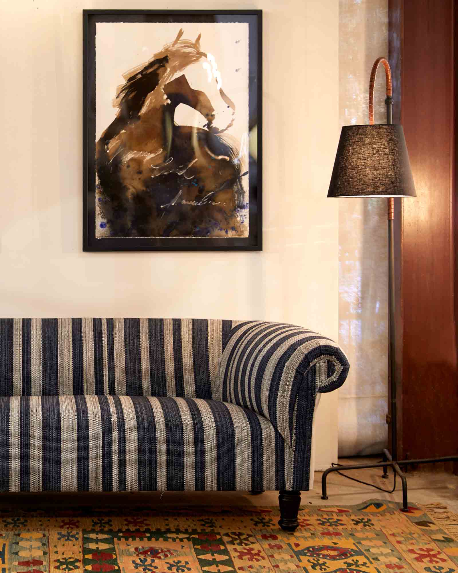  Upholstered sofa in blue and white fabric placed against a white wall with a horse painting hung up. Metal base floor lamp is beside the sofa and has a dark brown lamp shade.  