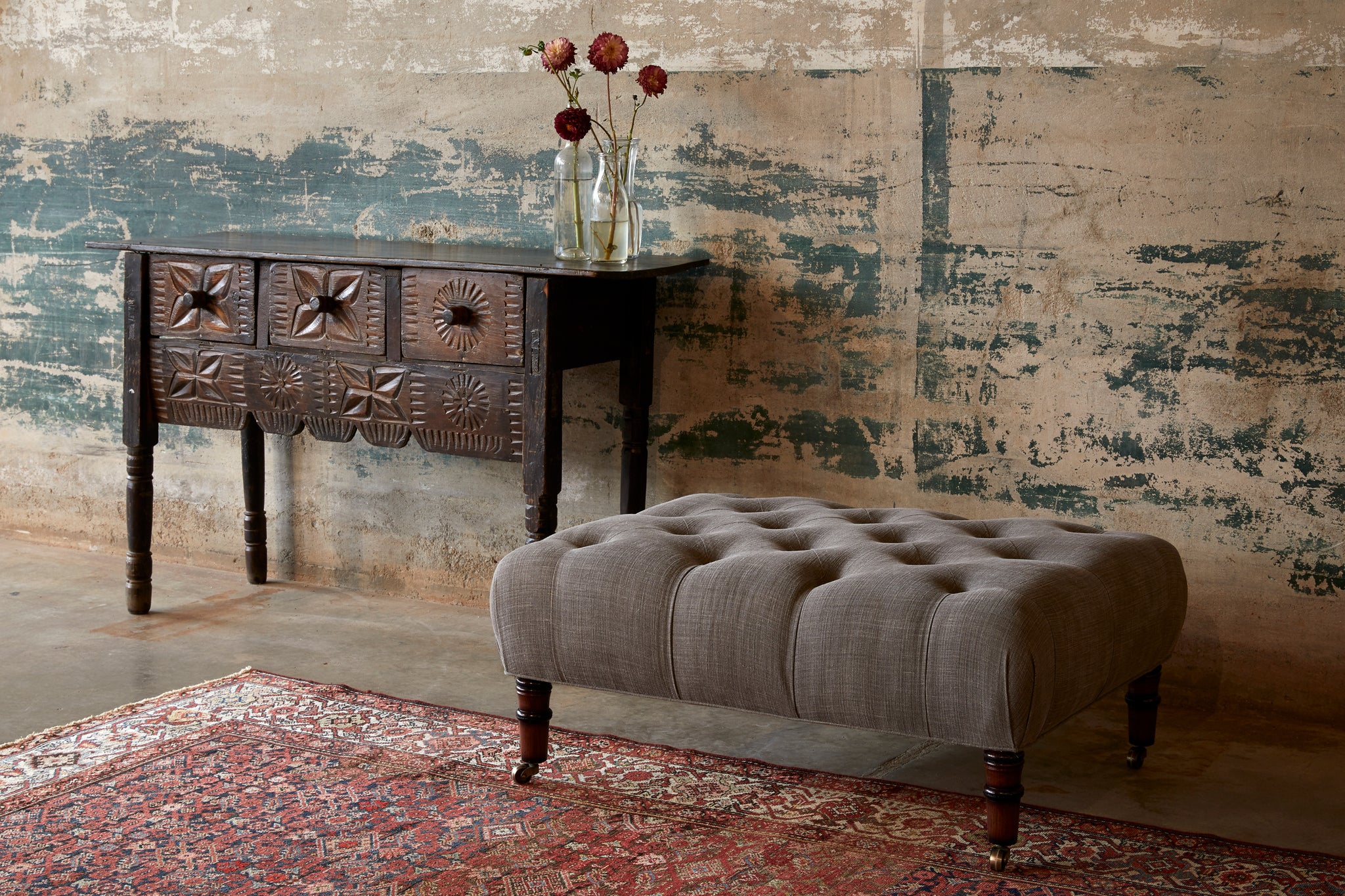  Field Ottoman in Rye Warm Grey next to a wood side table. Photographed in Rye Warm Grey. 