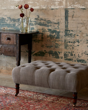  Field Ottoman in Rye Warm Grey next to a wood side table. Photographed in Rye Warm Grey. 