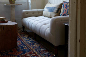  Field bench next to a wood coffee table, and a wood side table. On top of the bench are two patterned pillows. Photographed in Vintage Flax. 