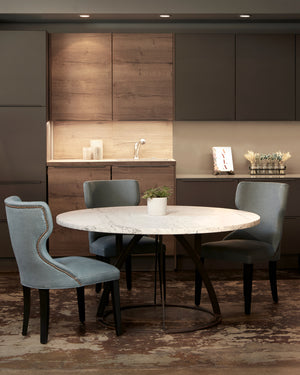  Three blue chairs around a round marble table. A wood and grey paneled kitchen in the background. Photographed on Bevard Ciel. 